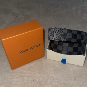 Svart och grå rutig bälte  - Snyggt bälte i svart och grått med rutigt mönster, levereras i originalförpackning. Bältet har en stilren design som passar till jeans eller kostymbyxor. Materialet är skinn och ger en exklusiv känsla. Perfekt för dig som vill ha en modern och trendig accessoar.