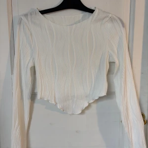Vit ribbad långärmad topp - Säljer en vit långärmad topp med vågigt ribbat mönster och asymmetrisk nederkant. Den är aldrig använd och säljs då den är förliten för mig 
