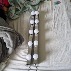 Sminkspegelbelysning med LED-lampor - Säljer två sminkspegelbelysningar med åtta runda vita LED-lampor på varje list. Lamporna sitter på en lång, rektangulär ram i silverfärgad metall och svart plast. Perfekt för att få jämnt ljus när du sminkar dig och skapa en riktig studiofeeling hemma.