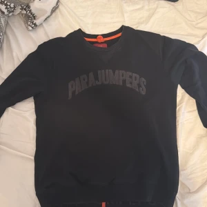 Svart sweatshirt från Parajumpers - Svart sweatshirt från Parajumpers med broderad logga över bröstet och klassisk rund hals. Tröjan har ribbade muddar och en orange detalj i nacken. Perfekt för dig som gillar stilrena och sportiga plagg med premiumkänsla.  Pris kan diskuteras vid snabbaffär