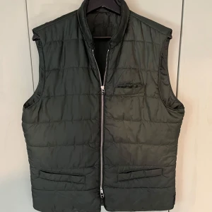 Mörkgrön dunväst från John Henric - Snygg mörkgrön dunväst från John Henric med quiltad design och hög krage. Väldigt fint skick, storlek L men sitter mer som M 