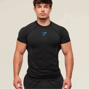 Svart Gymshark onyx - Säljer en svart Gymshark t-shirt i sportig modell med tight passform. T-shirten har korta ärmar, diskret mönstrad överdel och blå Gymshark-logga på bröstet. Materialet är lätt och andas, perfekt för träning och gym. Snygga detaljer på ryggen för extra stil.