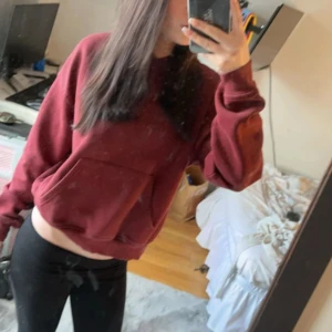 Vinröd hoodie med magficka - Säljer en vinröd hoodie med klassisk magficka och ribbade muddar. Tröjan har en loose passform och långa ärmar, perfekt för chill dagar. Färgen är djup vinröd och materialet känns mjukt och skönt mot huden.