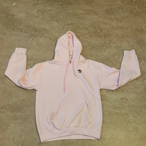 Ljusrosa hoodie från Remark med tryck - Säljer en ljusrosa hoodie från Remark med svart tryck av en narr på bröstet och stort tryck på ryggen. Tröjan har huva med snörning och en klassisk känguruficka framtill. Perfekt för dig som gillar streetwear och unika detaljer. Denna hoodie går inte heller att få tag på längre. Den är runt 1 år gammal men använd 1-2 gånger. Skriv gärna vid funderingar. Priset är inte heller hugget i sten! 