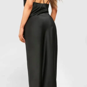 Svart långklänning från Boohoo - Säljer en svart långklänning från Boohoo i glansigt satin material. Klänningen har smala axelband och öppen rygg. Passformen är slim och tyget faller mjukt längs kroppen. Oanvänd!