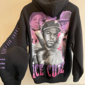 Svart Ice Cube hoodie med tryck - Säljer en svart hoodie från Ice Cube med stort grafiskt tryck i lila och rosa på ryggen och texten 'ICE CUBE' på bröstet. Ärmen har texten 'TODAY WAS A GOOD DAY' i lila. Klassisk huva med snörning och känguruficka framtill. 