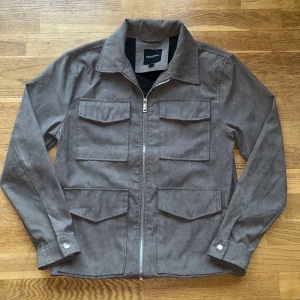 overshirt - Snygg grå overshirt från Brave Soul med fyra stora fickor framtill och dragkedja. Jackan har klassisk krage, långa ärmar med knapp vid ärmslut och är gjord i mocka.