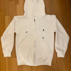 Vit Ralph Lauren hoodie med dragkedja - Säljer en stilren vit hoodie från Ralph Lauren med dragkedja och klassisk huva. Använd 1 eller 2 gånger och den är helt ren och i ett mycket bra skick. Storlek S, män. Skickar inom 1-3 dagar och pris kan diskuteras 