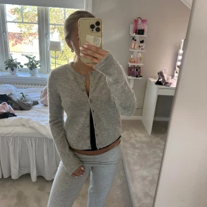 Ljusgrå stickad kofta med knappar - Mysig ljusgrå stickad kofta med rund hals och knäppning framtill. Koftan har långa ärmar och en rak, något croppad passform. Perfekt att slänga på sig över ett linne eller t-shirt för en chill look.