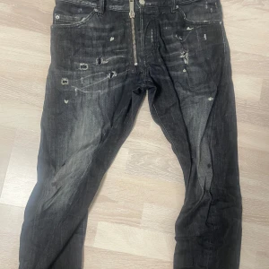 Svarta distressed jeans från Dsquared2 - Riktigt snygga svarta jeans från Dsquared2 med coola slitningar och distressed detaljer. Jeansen har en kraftig dragkedja framtill, klassisk femficksmodell och är tillverkade i bomull. Perfekta för dig som gillar en edgy streetstil. Storleken är 48 men passar mig som har 38 med ett skärp