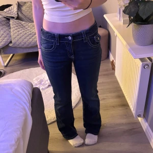 Mörkblå bootcut jeans med kontrastsömmar - Säljer ett par mörkblå jeans med bootcut passform och låg midja. Jeansen har tydliga vita kontrastsömmar, klassiska fem fickor och  detaljer på bakfickorna. 