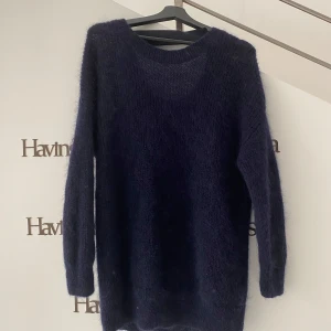 Mörkblå stickad tröja från COS - Mysig mörkblå stickad tröja med lång ärm och rund halsringning. Tröjan har en lätt transparent känsla och är fluffig i materialet, perfekt för lager på lager. Enkel och stilren modell som är lätt att matcha med olika outfits. Detalj med halvt öppen rygg 