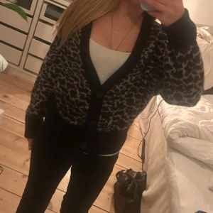 Leopardmönstrad kofta från & Other Stories - Säljer en supermjuk och snygg kofta från & Other Stories i leopardmönster. Koftan är svart och beige, har v-ringning, stora knappar framtill och långa ärmar. Perfekt för lager-på-lager och ger en cool vibe till din outfit.