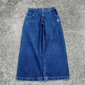 JNCO wide jeans med flames och kortlek - Blåa wide jeans från JNCO med riktigt breda ben och klassisk femficksdesign. På bakfickan finns en stor broderad kortlek med flames i rött och vitt, samt JNCO-logga. Jeansen är gjorda i kraftig denim och har en streetig vibe.