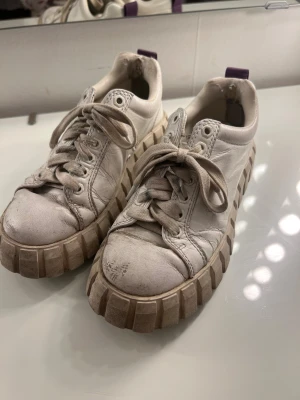 Chunky vita sneakers från Eytys - Säljer ett par chunky vita sneakers från Eytys med grov plattformssula och lila dragflik bak. Skorna har rund tå, snörning och är tillverkade i skinn. Skorna är väl använda men är inte ”förstörda” på något sätt💞