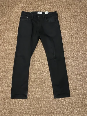 Svarta jeans från Jack & Jones - Svarta jeans från Jack & Jones med klassisk femficksdesign och smal passform. Jeansen har en enkel look utan synliga detaljer och är tillverkade i stretchigt jeansmaterial för extra komfort. Perfekt för dig som gillar stilrena byxor.