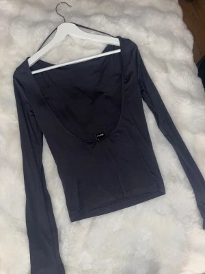 Mörkgrå open-back topp från Gina Tricot - Säljer en mörkgrå långärmad topp från Gina Tricot med öppen rygg. Modellen är slim och har en enkel, stilren design utan mönster eller detaljer. Materialet är deras soft touch och är väldigt stretchigt, perfekt för att skapa en clean look. Endast testad