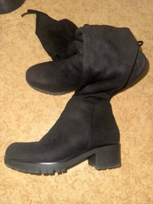 Svarta höga overknee stövlar med klack - Säljer ett par svarta overknee stövlar med låg klack. Stövlarna är gjorda i mocka imitation och har en dragkedja på sidan för enkel på och avtagning.