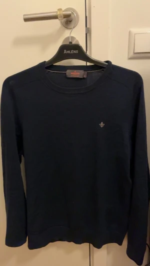 Mörkblå stickad tröja Morris - Snygg mörkblå stickad tröja från Morris med rund hals och diskret broderad logga på bröstet. Tröjan har långärmad passform och är perfekt för dig som gillar stilrena och klassiska plagg. Passar dig som vill ha en enkel men schysst look.