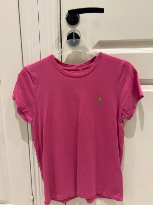 Rosa t-shirt från Polo Ralph Lauren - Snygg rosa t-shirt från Polo Ralph Lauren med klassisk grön broderad logga på bröstet. T-shirten har rund halsringning och korta ärmar. Aldrig använd endast tvättad 