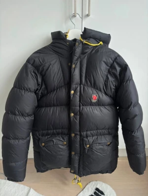 Svart dunjacka från Fjällräven XXS - Jättefin jacka från Fjällräven i storlek xxs, men skulle säga att den passar upp till S. Dock är dragkedjan lite trög för att tyget har gått sönder på ett ställe men går såklart fortfarande att stänga. Finns också några lagningar fast de syns knapp. I modell expedition down. Materialet är polyamid med fyllning av 90% dun och 10% fjäder. 