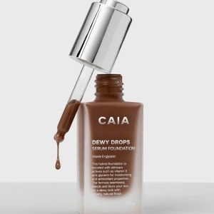 CAIA Dewy Drops Serum Foundation 50C - Serum foundation från CAIA i en djup brun nyans. Kommer i en stilren glasflaska med silvrig pipett för enkel applicering. Innehåller vitamin E och glycerin för återfuktning och ger en naturlig, daggig finish.