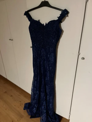 Marinblå lång spetsklänning med pärlor - Hej! Säljer min marinblåa balklänning då den inte passade och har därmed aldrig använts. Jättefin klänning med paljetter upptill och släp. Nypris 1400 