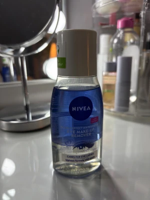 NIVEA Eye Make-Up Remover 125ml - NIVEA Double Effect Waterproof Eye Make-Up Remover, 125 ml. Tvåfasig formula med biotin som tar bort vattenfast smink och vårdar fransarna. Blå och genomskinlig vätska i plastflaska med vit kork. Perfekt för att ta bort ögonmakeup snabbt och skonsamt.