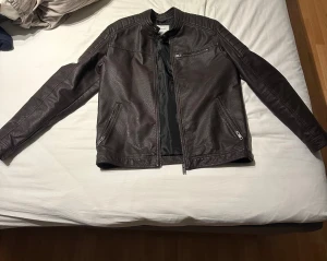 Brun skinnjacka Jack & Jones XL - Snygg brun skinnjacka från Jack & Jones i storlek XL. Jackan har klassisk bikerstil med ståkrage, dragkedja framtill och flera fickor med dragkedja. Materialet är skinnimitation med en cool textur och quiltade detaljer på axlarna. Perfekt för dig som gillar stilren och edgy look.