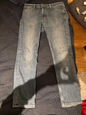 Blå jeans från Jack & Jones - Snygga blå jeans från Jack & Jones med klassisk femficksdesign och ljus tvätt. Modellen har raka ben och normal passform, med detaljerade sömmar och läderpatch bak i midjan. Perfekta för dig som gillar enkel och stilren denim. Byxorna är model Clark med regular fit, och i storlek W31, L32.