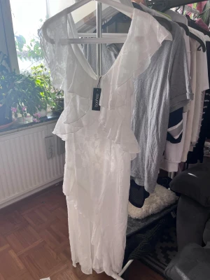 Vit blommig volangklänning från Boohoo - Storlek S/36/8 Supersöt långklänning från Boohoo i vit färg med blommigt texturerat mönster. Klänningen har volangdetaljer framtill och längs kjolen, v-ringad hals och korta ärmar. Materialet är lätt och känns som polyester, perfekt för sommarens alla tillfällen. Klänningen är slutsåld på deras hemsida!!! 