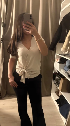 Beige omlottopp med knyt från Mango - Säljer en beige omlottopp från MNG Basics i storlek XS. Toppen har korta ärmar, v-ringad hals och snygg knytning framtill. Materialet är ribbad polyester som ger en cool struktur. Perfekt för dig som gillar stilrena och trendiga plagg.