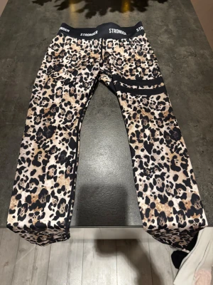 Leopardmönstrade leggings från Stronger - Snygga leopardmönstrade leggings från Stronger med bred svart midja och logga. De har en tight passform och är gjorda i stretchigt syntetmaterial som passar perfekt för träning. Färgerna går i beige, svart och bruna toner med coola svarta detaljer på benen.💞💞