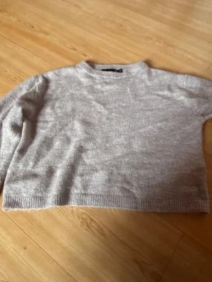 Beige stickad tröja från 157 XS - Mysig beige stickad tröja från 157 i storlek XS. Tröjan har en croppad passform, ribbade muddar vid hals, ärmslut och nederkant samt långärmade. Perfekt för dig som gillar enkel och clean stil.