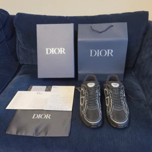 Svarta Dior B30 sneakers strl 44 - Säljer ett par svarta Dior B30 sneakers med coola vita detaljer och CD-logga på sidan och hälen. Skorna har en chunky platt sula, snörning och är gjorda i mesh och tekniskt tyg för en modern vibe. Perfekta för dig som gillar exklusiva och trendiga sneakers.
