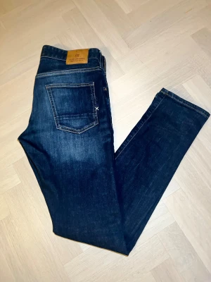 Scotch & Soda jeans  - Mörkblå jeans från Scotch & Soda, modell Ralston. Klassisk femficksdesign med kontrastsömmar och läderpatch bak. Tillverkade i bomull med lite stretch för extra komfort. Snygg passform och stilren look, perfekta till sneakers eller boots.