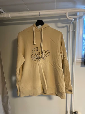 Official Gallery Hoodie – Storlek S - Säljer en beige hoodie från Official Gallery i storlek S. Hoodien har en avslappnad passform och ett stilrent streetwearuttryck med tryck på bröstet samt broderade detaljer vid ärmslutet.