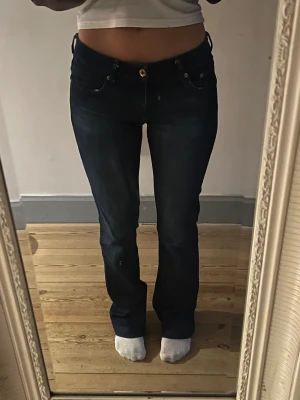 Mörkblå bootcut jeans - Säljer ett par mörkblå jeans med bootcut passform och snygga guldknappar på fickorna. Jeansen har låg midja och klassisk femficksdesign. Från hm, storlek 36/S, Innerbenslängd- 81