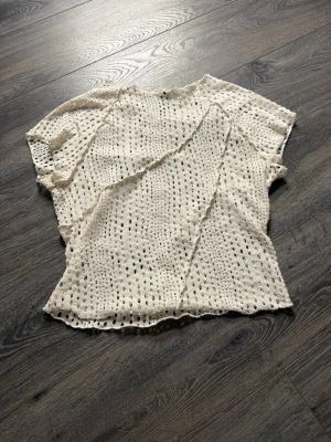 Vit virkad blus med hålmönster - Säljer en vit blus från H&M med korta ärmar och ett snyggt hålmönster över hela plagget. Materialet känns luftigt och lätt, vilket gör den superbekväm att bära.