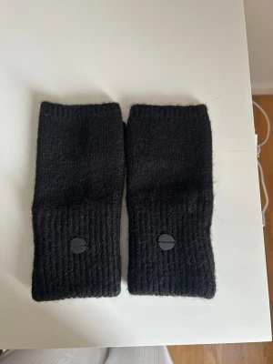 Vantar - Säljer ett par svarta stickade handledsvärmare från Superdry. De är ribbstickade och har tumhål, vilket gör dem perfekta för dig som vill ha fria fingrar men ändå hålla händerna varma. Diskret logga på ena sidan.