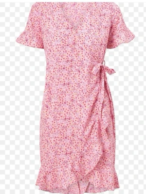 Rosa blommig omlottklänning strl. L - Rosa omlottklänning från Vero Moda med blommigt mönster. Klänningen har korta ärmar med volanger, samt volangkant nertill och även knyt i midjan. V-ringad och lätt figurnära form. Endast använd ett fåtal gånger, ser ut som ny.