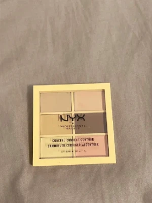 NYX Conceal Correct Contour Palette - Säljer en NYX Conceal Correct Contour-palett med sex krämiga nyanser för att täcka, korrigera och skulptera ansiktet. Färgerna varierar från beige, gul, grön, rosa till bruna toner. Perfekt för att skapa en jämn bas och highlighta eller dölja ojämnheter.