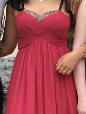 Röd långklänning med glittrig detalj - Säljer en röd långklänning med glittrig kant upptill och omlott-detalj över bysten. Klänningen har ett fint fall i kjolen, perfekt för speciella tillfällen. Materialet känns lätt och följsamt.