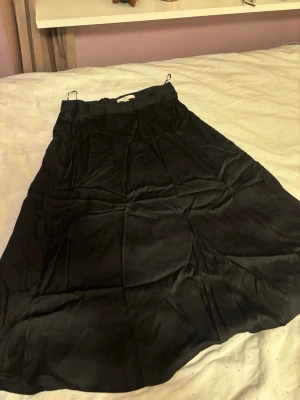 Svart långkjol satin från Esprit - Säljer en svart långkjol från Esprit i storlek 36. Kjolen har en enkel och stilren design med lätt glansigt tyg och dragkedja i sidan. Perfekt för dig som gillar klassiska plagg med en clean look.