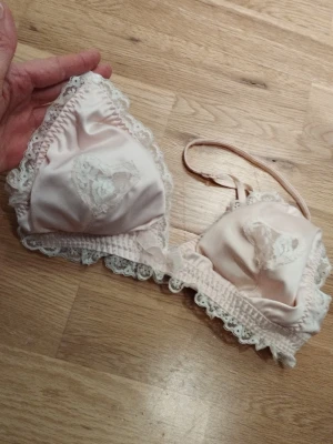 Ljusrosa spetsdetaljerad bralette - Supersöt ljusrosa bralette i satinliknande material med spetskant och hjärtformad spetsdetalj på kuporna. Justerbara axelband och liten rosett framtill samt utdragbara inlägg. Sockersöt helt helt! Perfekt för alla hjärtans dag  / Valentine's day. Jag har fler annonser uppe och ger mängd rabatt, så kolla gärna min sida!