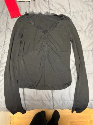 Svart ribbad topp med spets från SHEIN - Säljer en svart långärmad topp från SHEIN i ribbat material. Toppen har v-ringning med spetsdetaljer och en snygg rynkning framtill. Storlek S