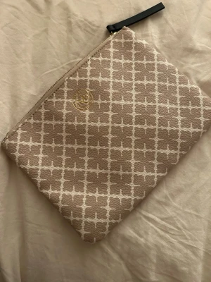 Oanvänd, Beige kuvertväska från By Malene Birger - Säljer en beige och vit kuvertväska från By Malene Birger med klassiskt rutigt mönster och guldfärgad logga. Väskan har dragkedja upptill och svart läderdetalj på zip-pullern. Perfekt för att bära det viktigaste.