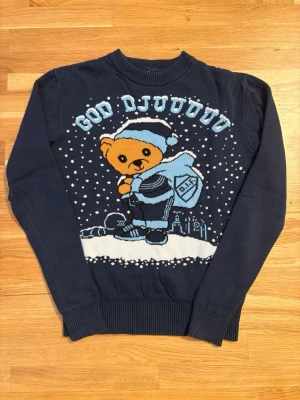 Blå jultröja DIF med björnmotiv - Säljer en mörkblå jultröja från DIF med ett gulligt björntryck på framsidan och texten 'God Djul'. Passar 150-165 cm i längd, dvs storlek S-liten M. Sparsamt använd, därav i super bra skick. 