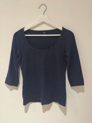 Mörkblå topp från H&M med 3/4-ärm - En enkel och stilren mörkblå topp från H&M i storlek S. Toppen har rundad urringning och trekvartsärm. Tillverkad i mjuk bomull som känns skön mot huden. Perfekt att matcha med jeans eller kjol för en clean look.