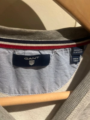 Grå sweatshirt från GANT, stl 158/164 - Klassisk grå sweatshirt från GANT med rund halsringning och broderad logga på bröstet. Tröjan har ribbade muddar vid ärmslut och nederkant. Tröjan är bra slitet vid armbågen, men syns inte när man använder tröjan. 